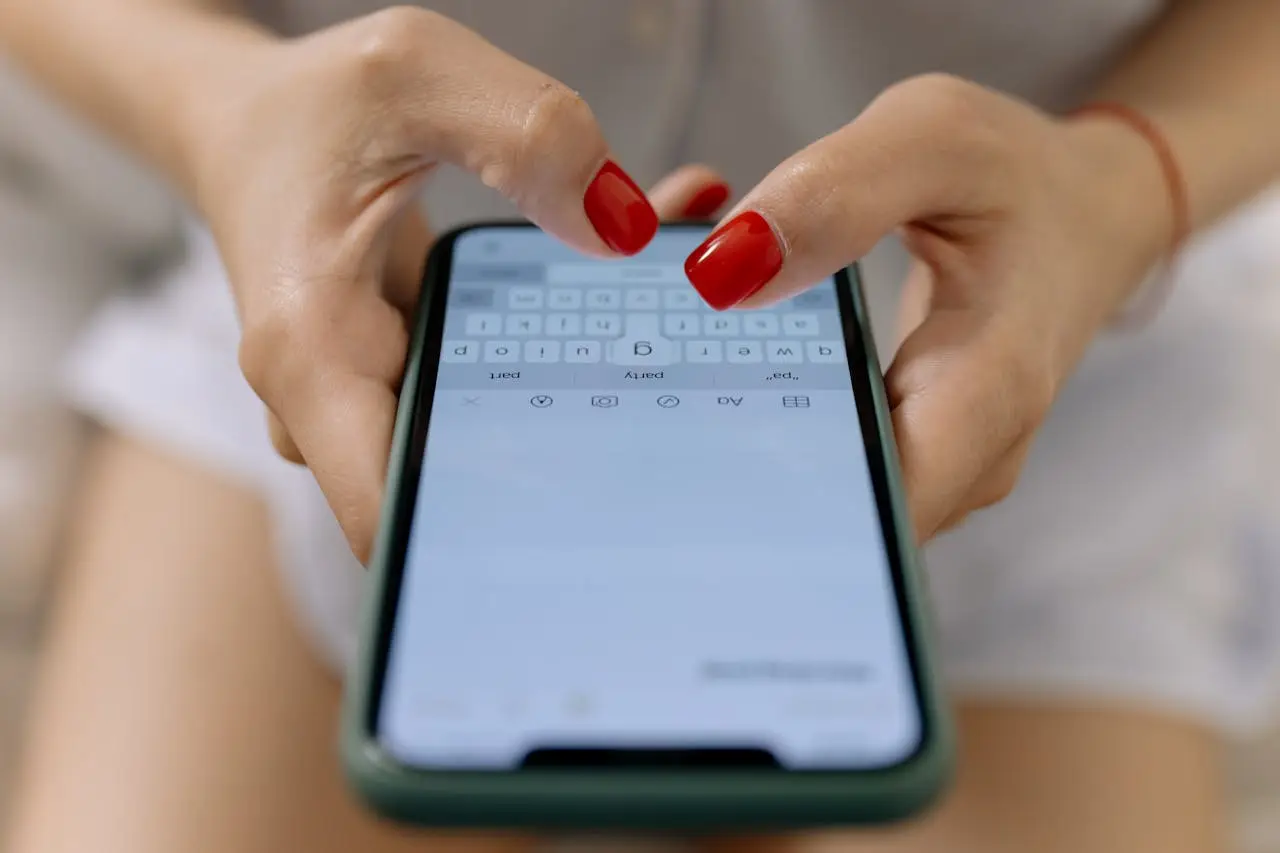 woman with red nail polish wearing white shorts, sitting, typing on iphone.
